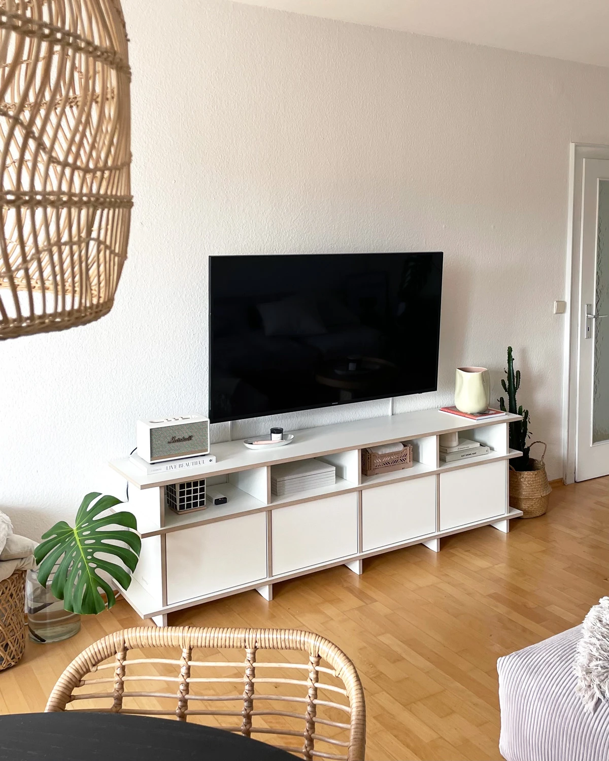 Meuble TV bas blanc droit avec portes, compartiments ouverts, télévision et décoration dans un salon lumineux
