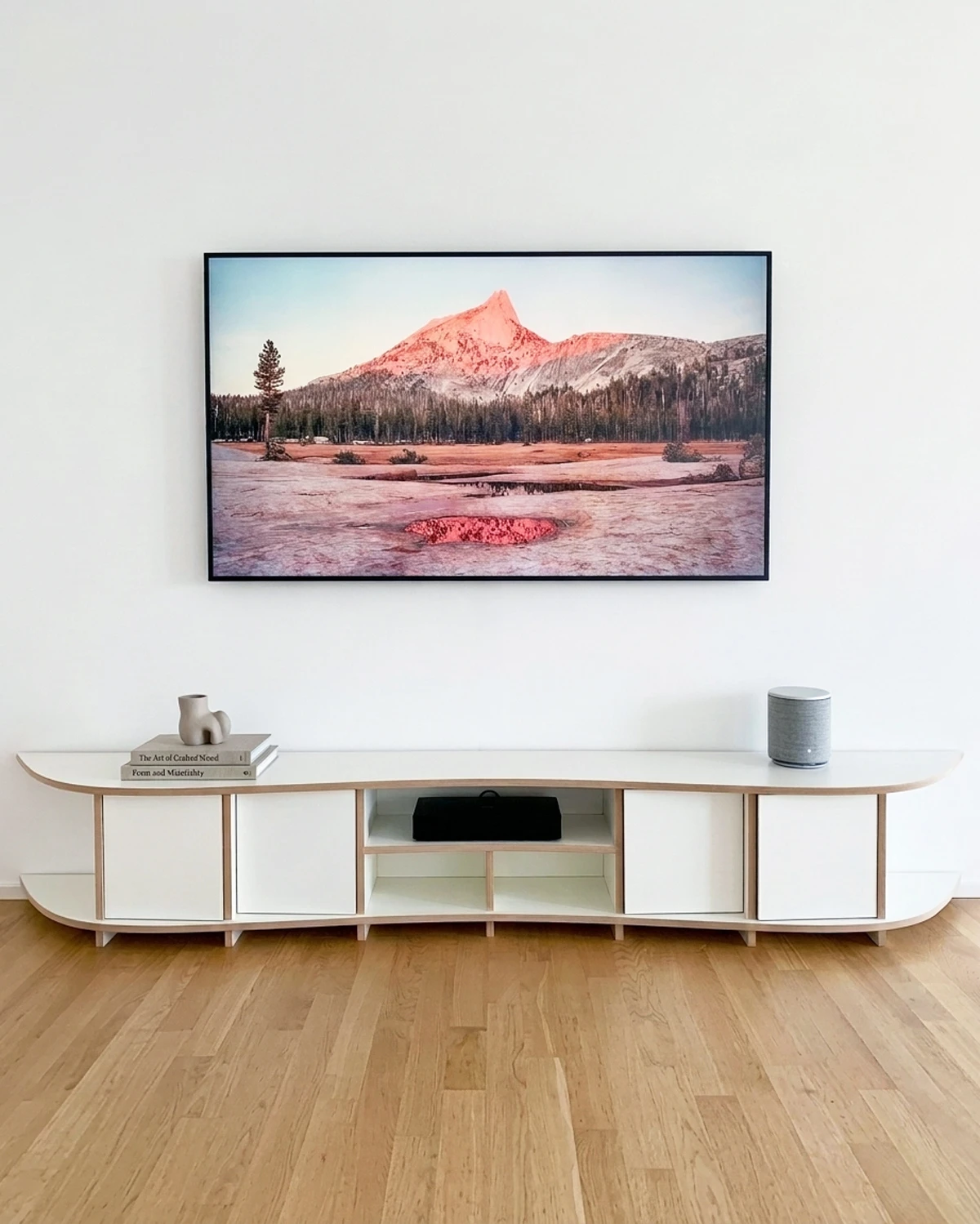 Meuble TV bas blanc ondulé avec portes, compartiments ouverts, télévision et décoration dans un salon lumineux