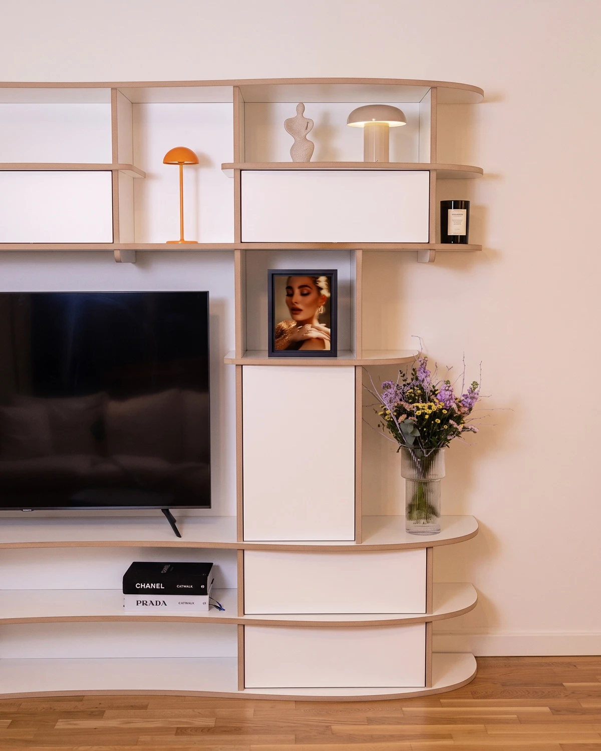 Meuble TV mural blanc sur mesure avec coins arrondis, niches ouvertes, placards fermés et télévision intégrée de sophieberna