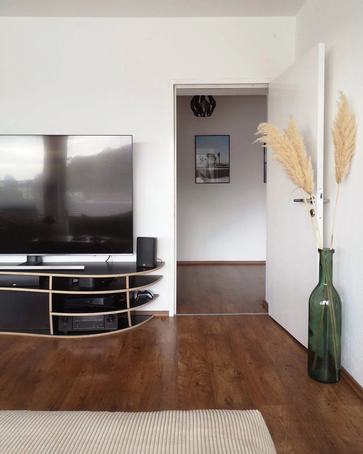 Meuble TV bas organique noir avec chant bois, télévision, appareils hi-fi et décoration dans un salon lumineux