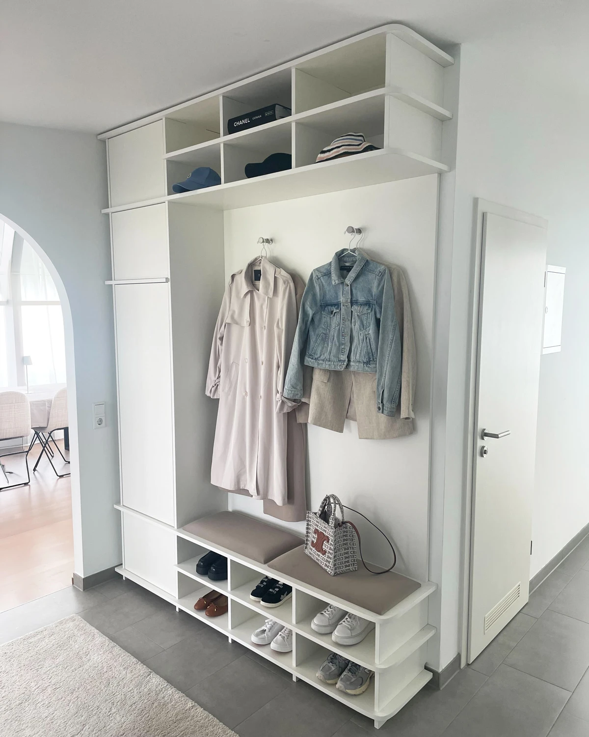 White hallway wardrobe in a corner with integrated bench, hooks, shoe storage, open compartments and storage in a bright hallway